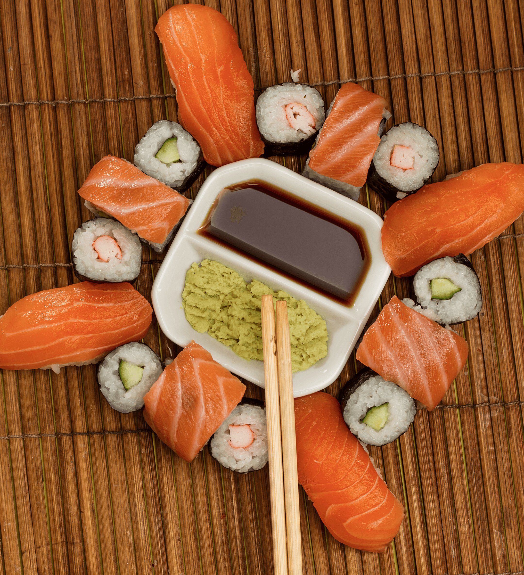 Lachs-Nigiri und Maki um eine Schale mit Sojasauce und Wasabi auf einer Bambusmatte.