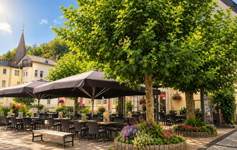 Die Außengastronomie des Eiscafés San Remo mit Sonnenschirmen unter einem großen Baum